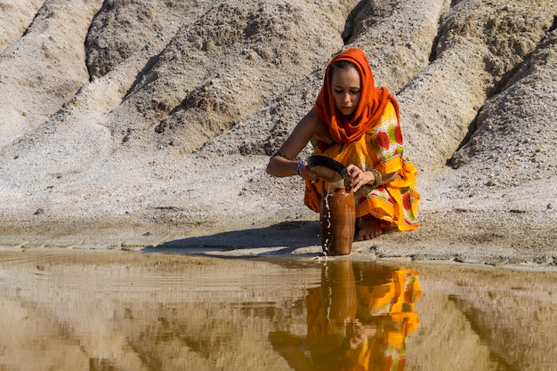 동양적인 외모의 소녀는 건조한 지역의 더러운 근원에서 물을 투수에 채운다
