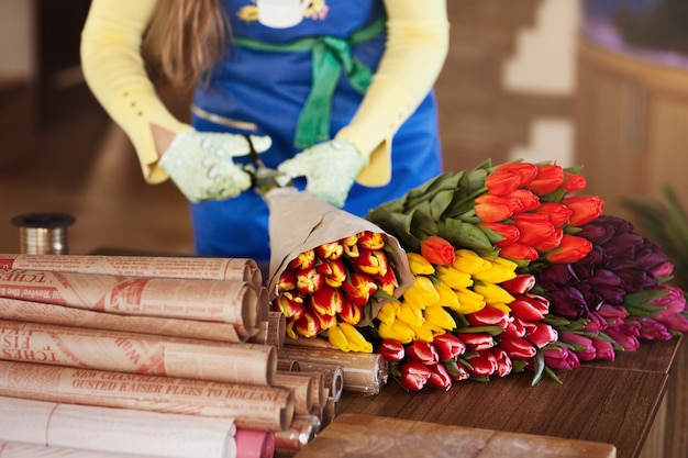 Girl packs colorful bouquets of tulips in craft paper