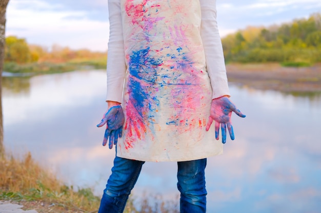 Girl in painted apron with dirty hands. Female artist outdoors