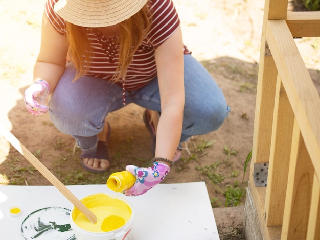 女の子の画家は、バケツで黄色と白の絵の具を混ぜ合わせ、アクリルのファサードの絵の具を混ぜ合わせます