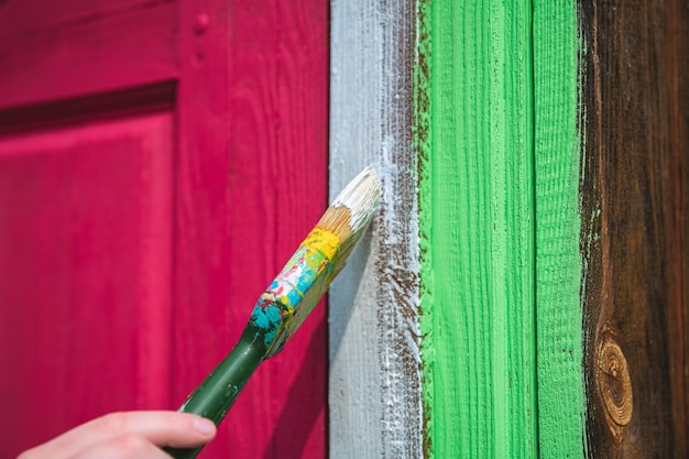 Photo girl painting the door of a wooden house in a bright purple viva magenta color