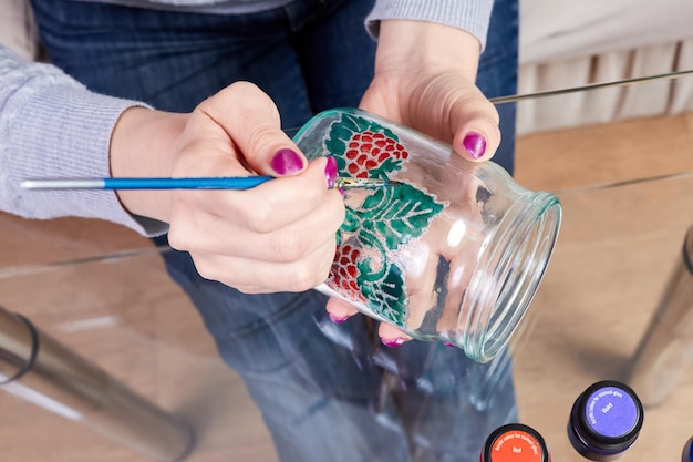 A girl paints a glass jar with stained glass paints