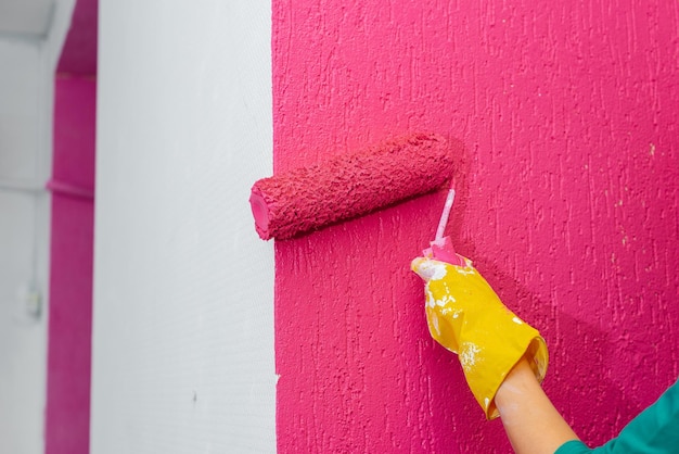 한 소녀가 새 아파트에서 분홍색 롤러로 벽을 클로즈업으로 칠하고 있습니다. 인테리어 및 새 아파트의 개조 집들이와 바람직한 모기지