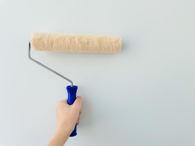 La ragazza dipinge il muro con la mano femminile della vernice bianca con il rullo della pittura della parete si chiuda con lo spazio della copia