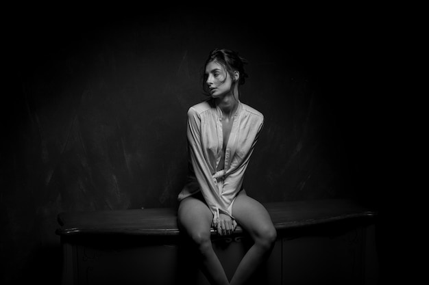 A girl in panties and a white shirt posing in a vintage interior black and white photo