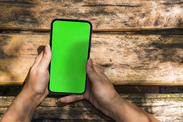 Girl in the park holding a smartphone with green screen app on the screen Rustic wooden table Chroma Key