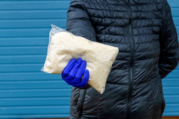 The girl passes rice at arm\'s length in a glove. help during a\
pandemic. donations of food or the concept of food delivery.