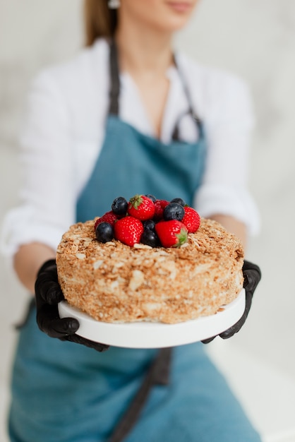 ベリーの甘い食べ物と蜂蜜ケーキを保持している女の子のパティシエ