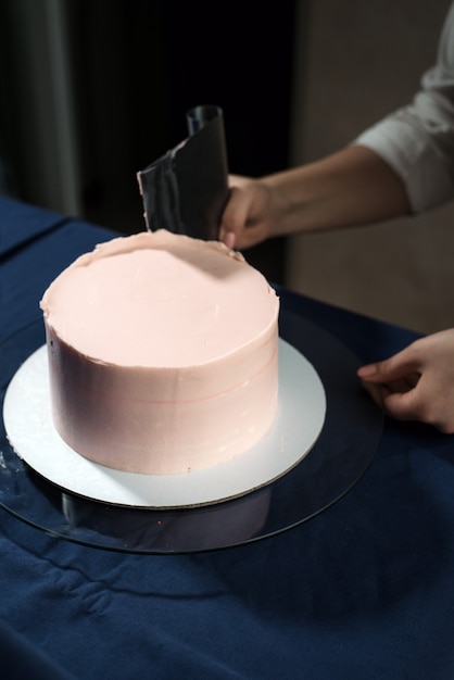 Ragazza pasticcera, fa una torta nuziale con le proprie mani e spreme la crema sugli strati di torta.