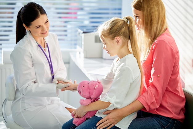 Girl patient at usual medical inspection checkup, friendly affable doctor and patient in clinic, female pediatrician holding hand of girl, smile. medicine, healthcare concepts