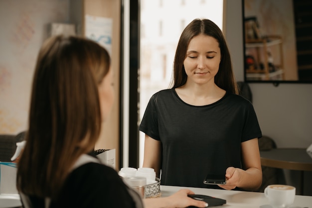 A girl paying for her coffee with a smartphone by contactless NFC technology in a cafe