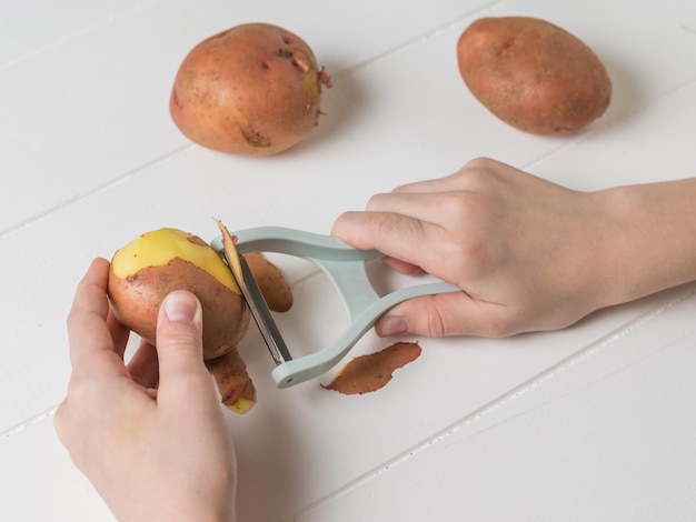 女の子は特別な灰色のナイフでジャガイモをはがします。野菜を傾ける特別な機器。