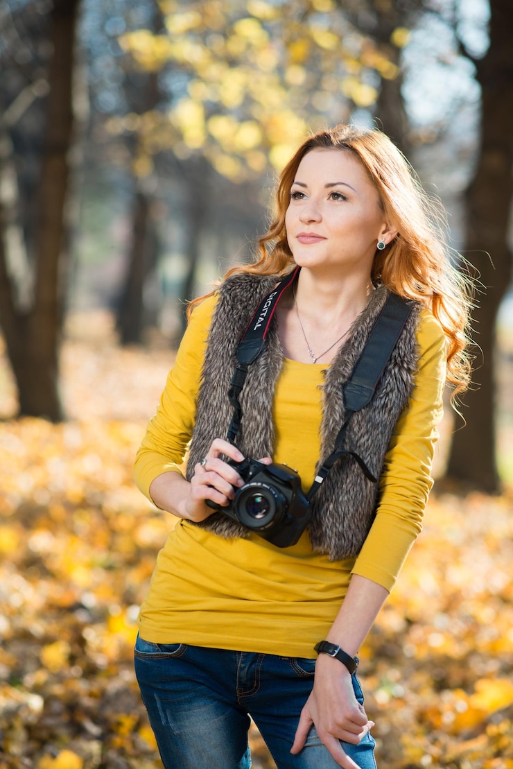 カメラを持った女の子の写真家が秋の公園で写真撮影をします