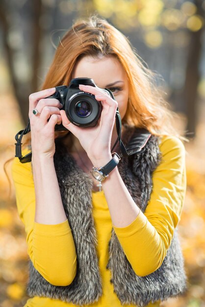 カメラを持った女の子の写真家が秋の公園で写真撮影をします