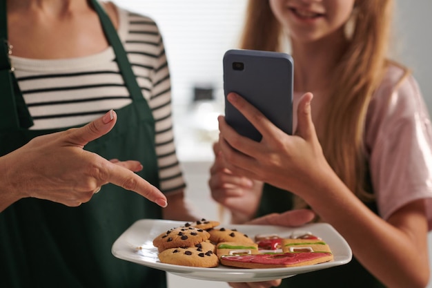 写真 ソーシャルメディアに投稿を共有するために母親と一緒に焼いたクッキーを載せたプレートを撮影する女の子