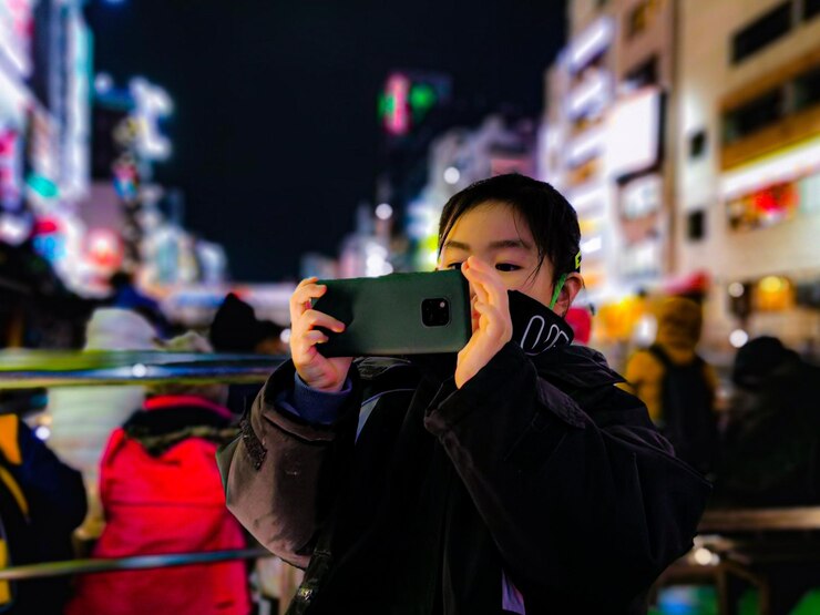 Photo 夜街で携帯電話で写真を撮っている少女