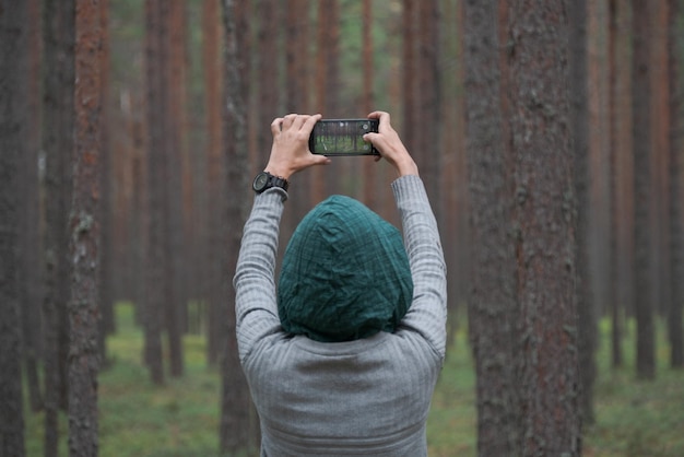 The girl photographs the forest with a mobile phone Back view