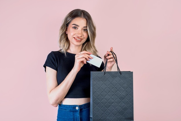 A girl on a pink background with a black paper bag shopping concept bank or discount card mockup