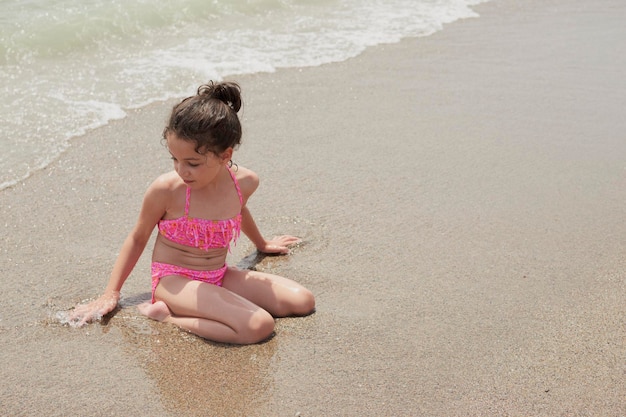 Girl in a pink bikini playing happily on the shore of the beach with the waves on a sunny summer day Vera Spain