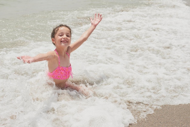 Ragazza in un bikini rosa che gioca felicemente sulla riva della spiaggia con le onde in una soleggiata giornata estiva vera spagna