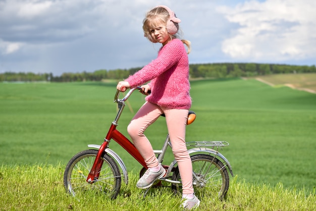 Girl in pink clothes rides a bicycle on the field.