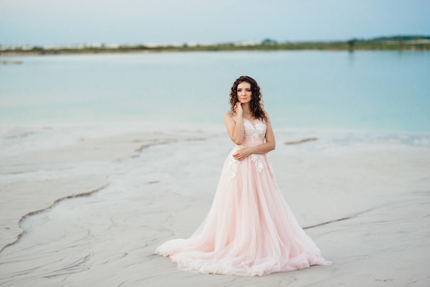 ピンクのドレスを着た女の子が砂漠の白い砂浜を歩いている