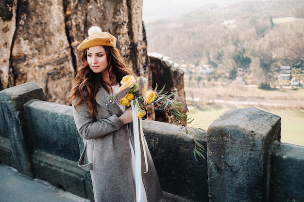 A girl in a pink dress and hat with a bouquet of flowers against the background of mountains and gorges in Swiss Saxony, Germany, Bastey.