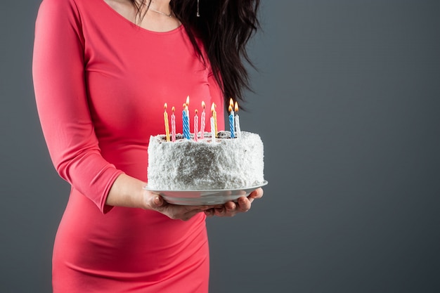 A girl in a pink dress holds in her hands a cake with burning candles, close-up. Happy birthday congratulation celebration party anniversary. Copy space.