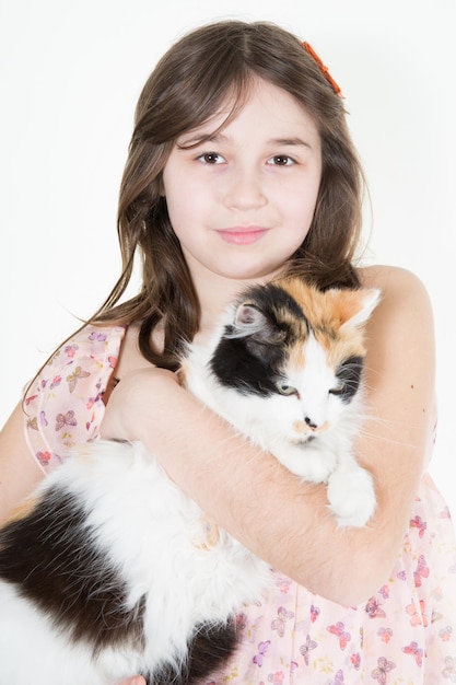 Girl in pink dress holds a red cat standing on white background