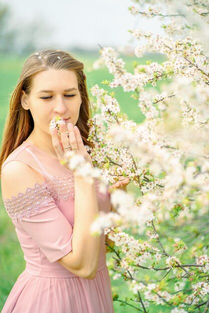 a girl in a pink dress sniffs a flowering branch