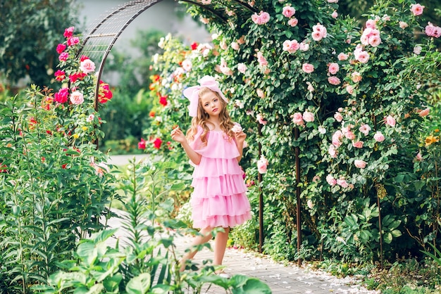 Girl in a pink dress with a bow on her head in the rose garden. Girl doll