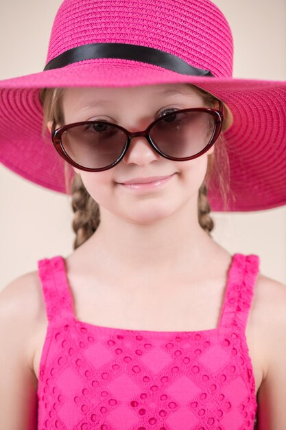 Photo a girl in a pink hat and sunglasses smiles.