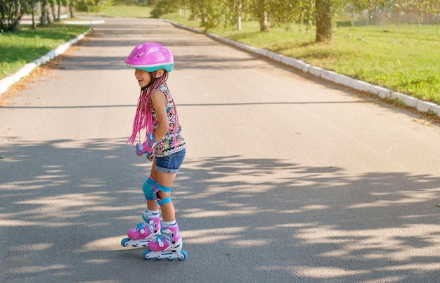 Photo girl in a pink helmet and sports equipment for safe roller skating laughs merrily while riding