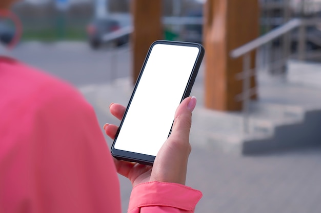 Girl in a pink jacket holds a smartphone mockup with white screen in hands. Mock-up Technology.