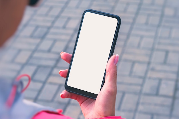 Girl in a pink jacket holds a smartphone mockup with white screen in hands. Mock-up Technology.