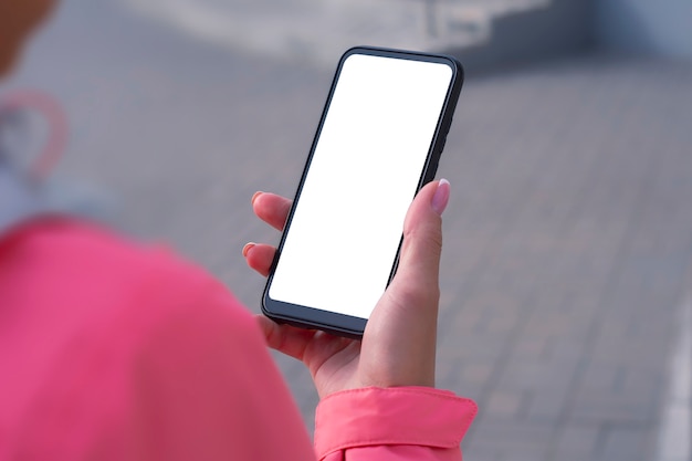 Girl in a pink jacket holds a smartphone mockup with white screen in her hands.