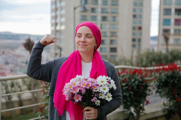 Girl in pink scarf and white mask with daisies outdoors. Cancer awareness concept.