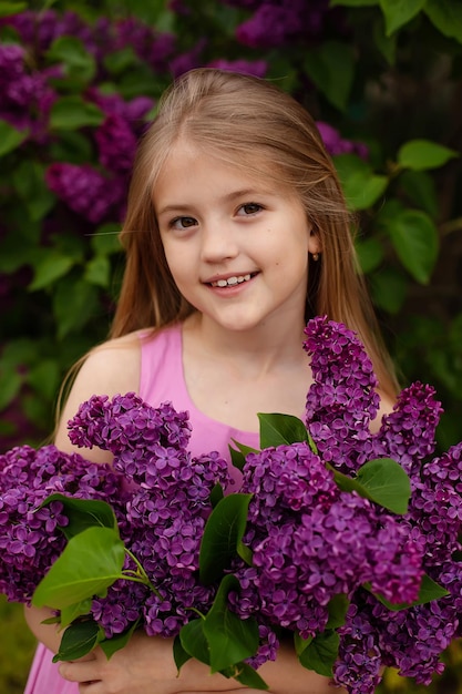 A girl in a pink shirt holds a bunch of purple lilacs.