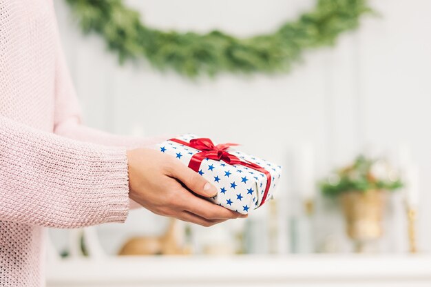 Una ragazza in un maglione rosa, tiene tra le mani un regalo con stelle blu e un nastro rosso. su uno sfondo chiaro. concetto sul tema delle vacanze.