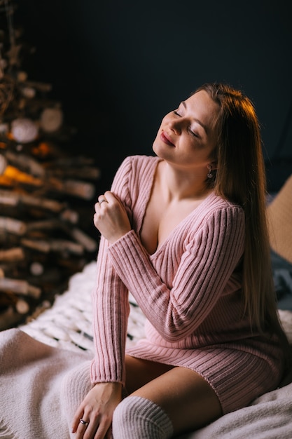 Девушка в розовом свитере сидит на кровати с закрытыми глазами Наслаждайтесь праздничным вечером
