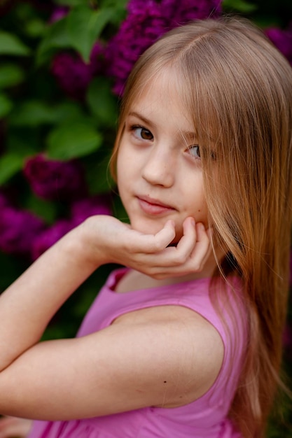 A girl in a pink tank top stands in front of purple flowers.