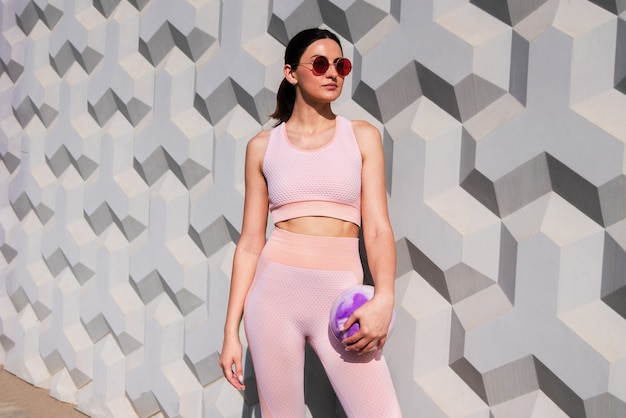 A girl in a pink tracksuit stands with a training ball near the wall