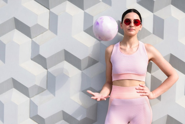 Девушка в розовом спортивном костюме стоит с тренировочным мячом у стены
