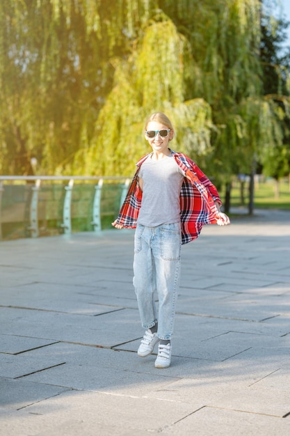 A girl in a plaid shirt jumps and runs along a path in a city park on a sunny summer day Teenage holiday concept