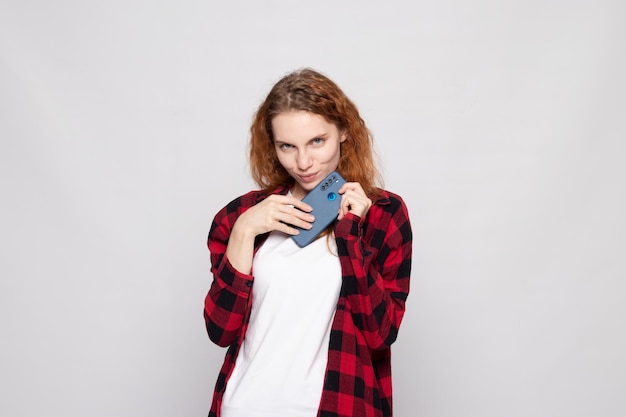 Photo girl in a plaid shirt on a light background with a smartphone