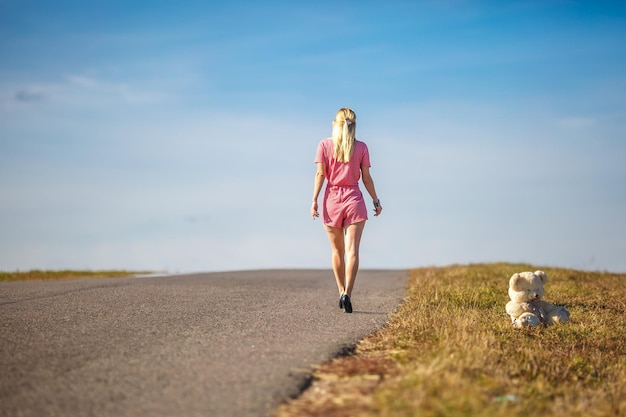 Girl in plaid suit leaves on asphalt road from teddy bear concept of ending childhood