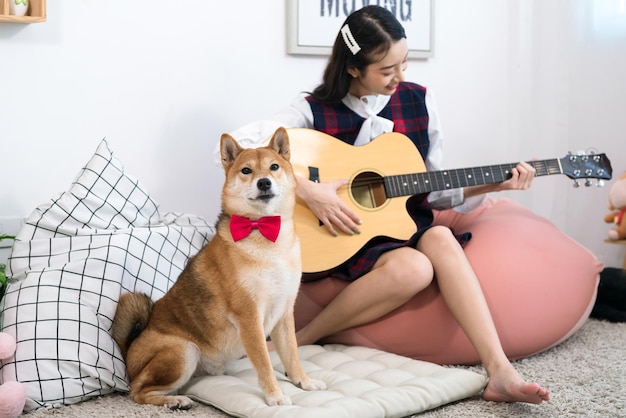 사진 색 거실에서 시바 이누 개와 기타를 연주하는 소녀 시바 이뉴 개와 연주하는 젊은 여성