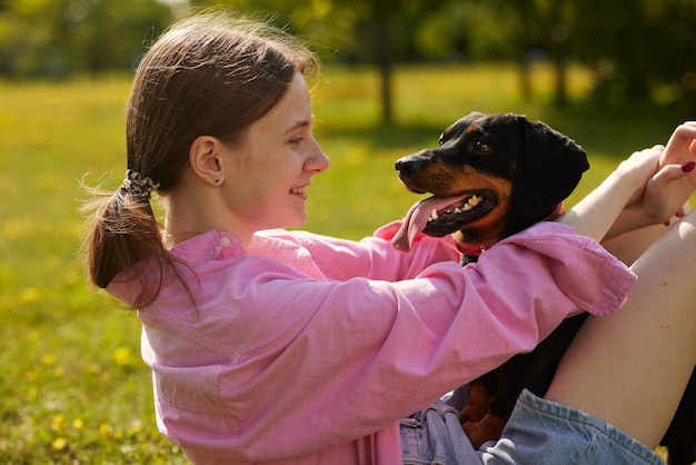 girl playing and hugging dachshund dog on green lawn dog care concept