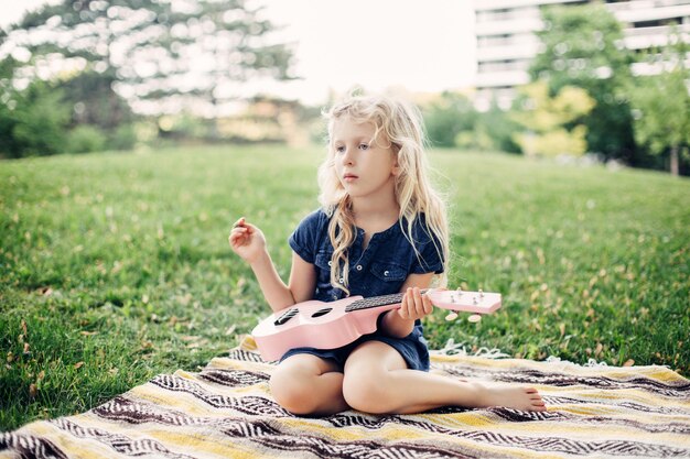 Girl playing pink guitar toy outdoor child playing music and singing song in park music hobby