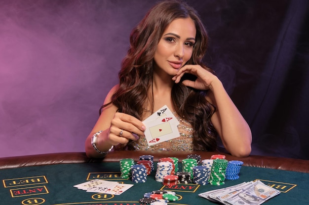 Ragazza che gioca a poker al casinò che mostra le carte sedute al tavolo con pile di fiches e denaro fumo nero